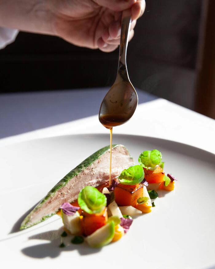 Sauce versée à la cuillère sur un plat de légumes colorés finement dressé